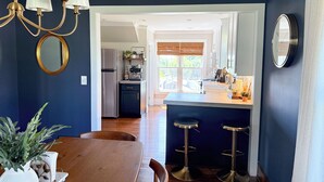Une cuisine moderne aux murs bleu foncé, avec une table à manger en bois et un coin bar doté de tabourets.