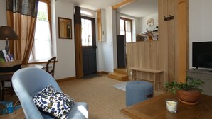 A living room with a blue armchair, a wooden coffee table, a TV, and a potted plant. - Village house in the Perche (Le Mage)