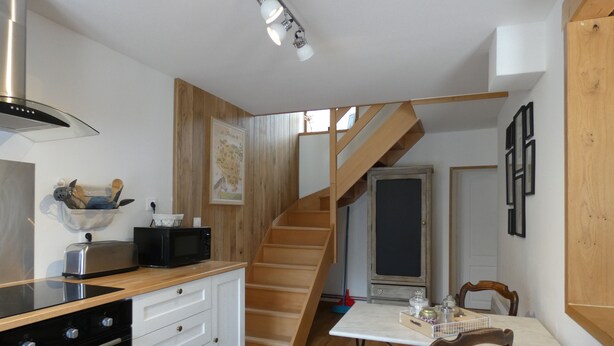 A compact kitchen with a wooden staircase, a dining table with chairs, and a microwave. - Village house in the Perche (Le Mage)