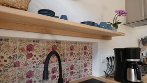 A kitchen with a black faucet, a coffee maker, and a floral backsplash. - Village house in the Perche (Le Mage)