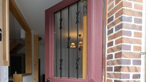 A red door with a glass panel and a brass handle, leading to a brick wall and a wooden staircase. - Village house in the Perche (Le Mage)