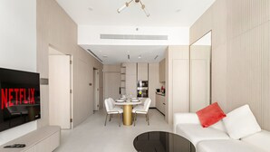 Uma sala de estar moderna com televisão de tela plana, um espaço de refeições com mesa redonda e um sofá com almofada vermelha.