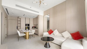 Uma sala de estar moderna com um sofá branco, uma mesa de centro redonda e uma área de jantar com mesa e cadeiras brancas.