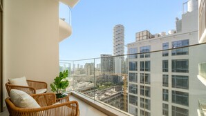 Uma varanda com móveis de vime, um vaso de planta e vista para a cidade.