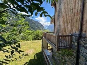 Ein Holzhaus mit einer Steinwand, einem Holzbalkon und Blick auf eine gebirgige Landschaft.