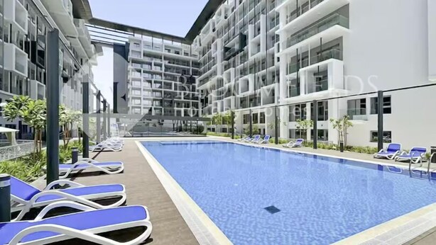 A modern building with a swimming pool, sun loungers, and a clear sky.