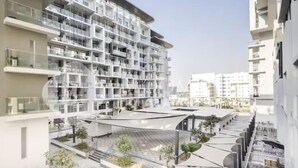 A modern multi-story building with balconies, a central courtyard, and surrounding greenery.