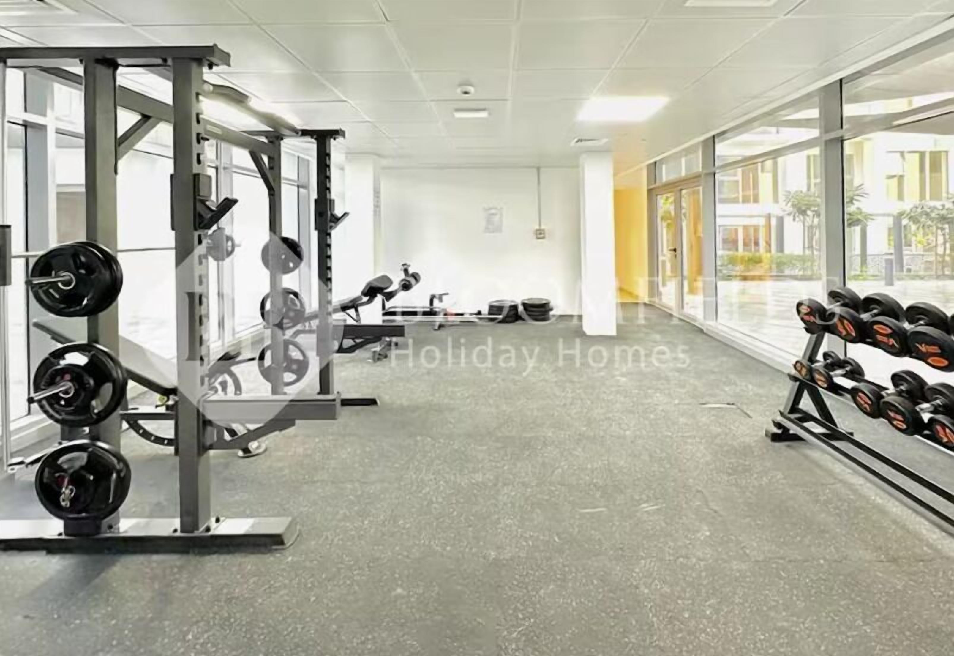 Une salle de sport équipée de matériel de musculation, dotée de grandes fenêtres et présentant un design moderne et épuré.