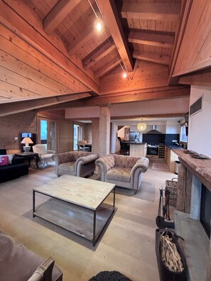 A spacious living area with a high ceiling, wooden beams, and a cozy fireplace. There are comfortable sofas and a coffee table. - Charming duplex apartment in Courchevel Le Praz, 4 bedrooms. (Courchevel)