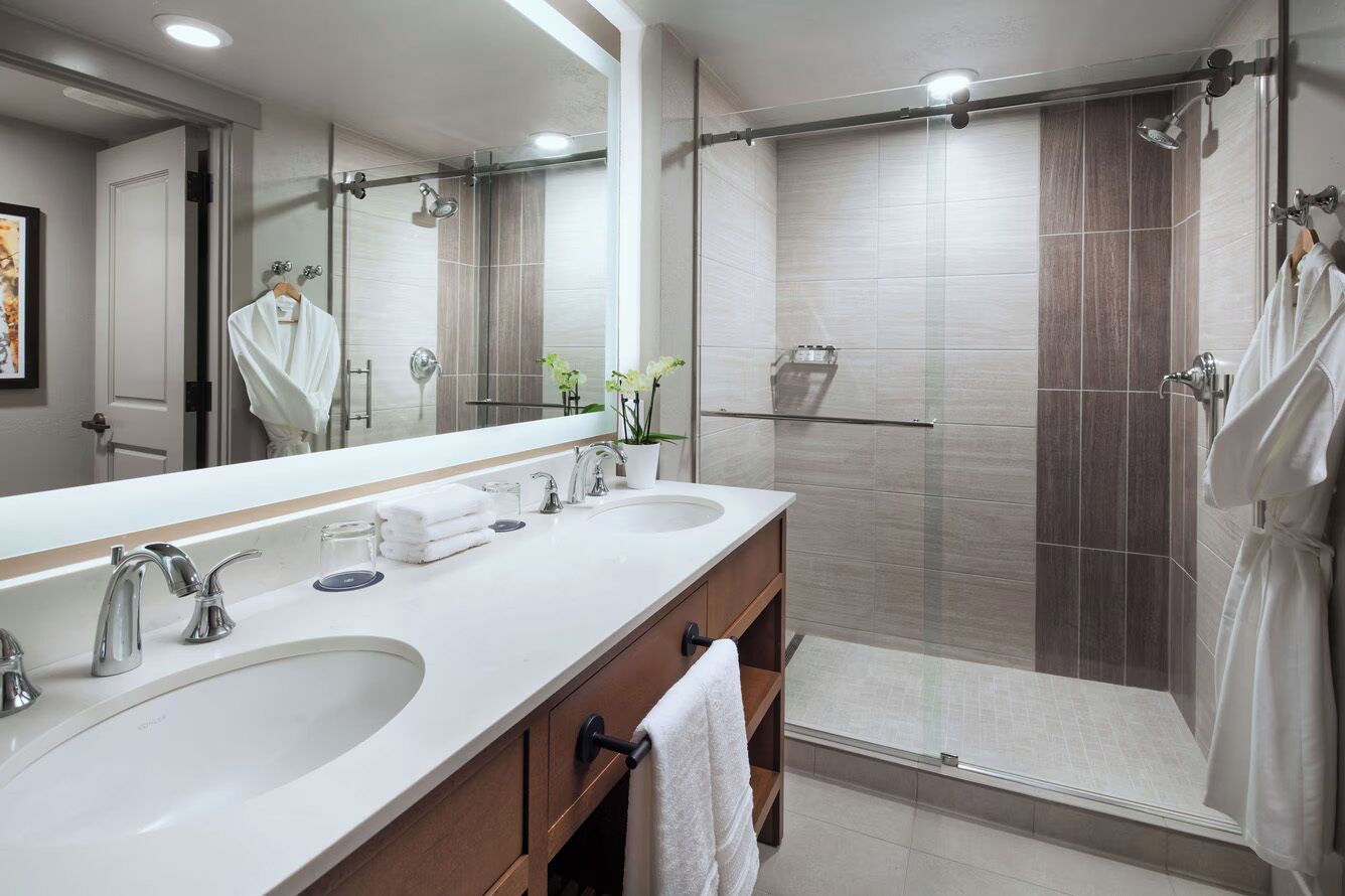 Une salle de bain moderne avec deux vasques, un grand miroir et une douche séparée par une paroi de verre.