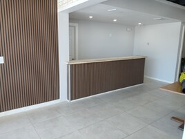 Uma área de recepção moderna com design em painel de madeira, piso ladrilhado e uma porta branca ao fundo.