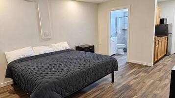 A bedroom with a bed, a nightstand, and a wooden floor.