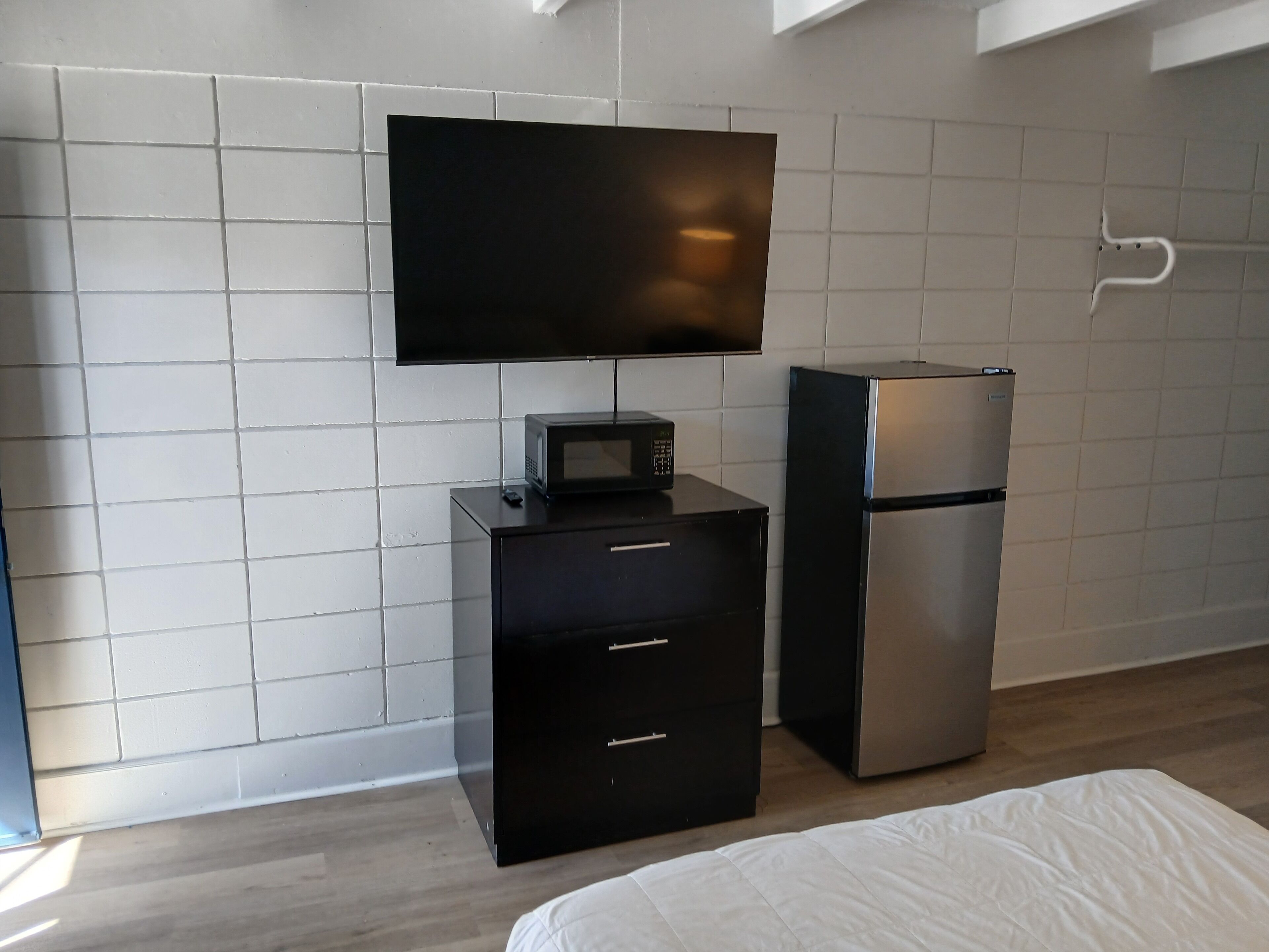 A modern room with a flat-screen TV mounted on the wall, a black minibar with a microwave, and a silver refrigerator.