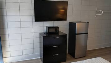 A modern room with a flat-screen TV mounted on the wall, a black minibar with a microwave, and a silver refrigerator.