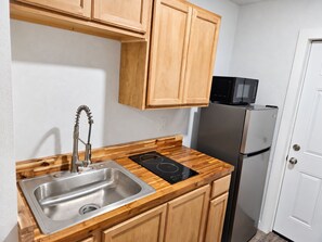 A kitchen with wooden cabinets, a stainless steel sink, a black induction cooktop, and a black refrigerator.