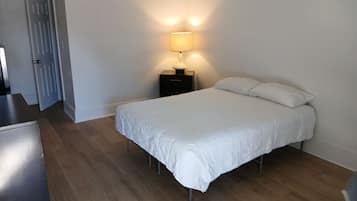 A bedroom with a bed, a nightstand with a lamp, and a door.