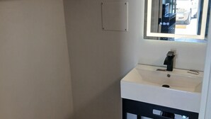 Ein kleines Badezimmer mit einem weißen Waschbecken, einem Spiegel und einem schwarzen Regal.