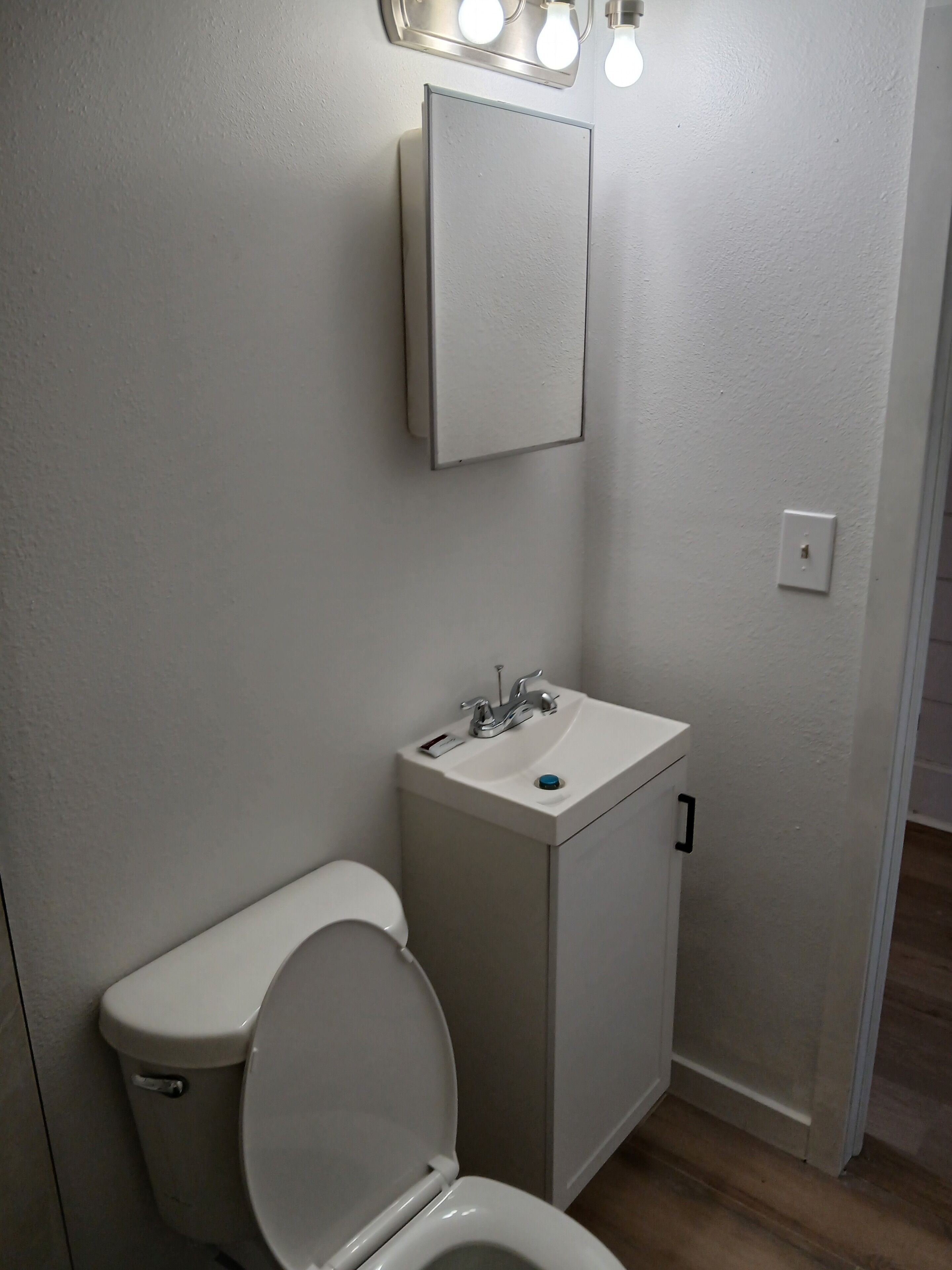 A small, white bathroom with a toilet, sink, and mirror.