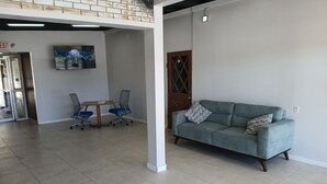 Ein geräumiges Wohnzimmer mit grauem Sofa, zwei Bürostühlen, einem Holztisch und einem an der Wand befestigten Fernseher.