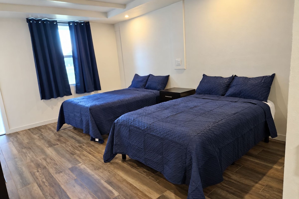 A hotel room with two beds, a window with curtains, a nightstand, and a wooden floor.