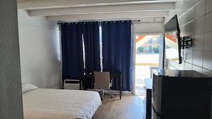 Ein Hotelzimmer mit Bett, Schreibtisch, Stuhl, Fernseher und einem großen Fenster mit Vorhängen.