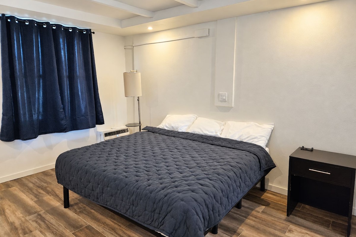 A bedroom with a bed, a bedside table, a lamp, and a window with curtains.