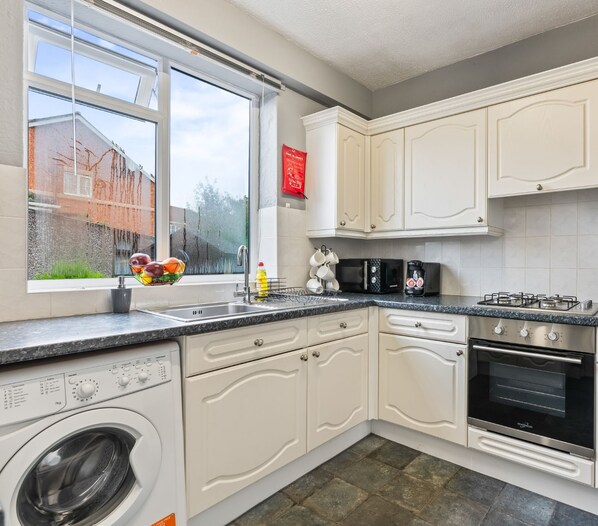 A kitchen with white cabinets, a washing machine, a microwave, a gas stove, and a built-in oven.