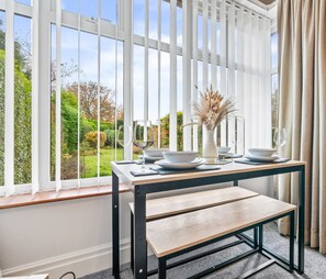 A modern room with a large window, a dining table set with white plates and bowls, a bench, and a vase with dried plants.