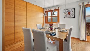 Un coin repas avec une table en bois dressée pour quatre personnes, des chaises blanches et un tableau accroché au mur.