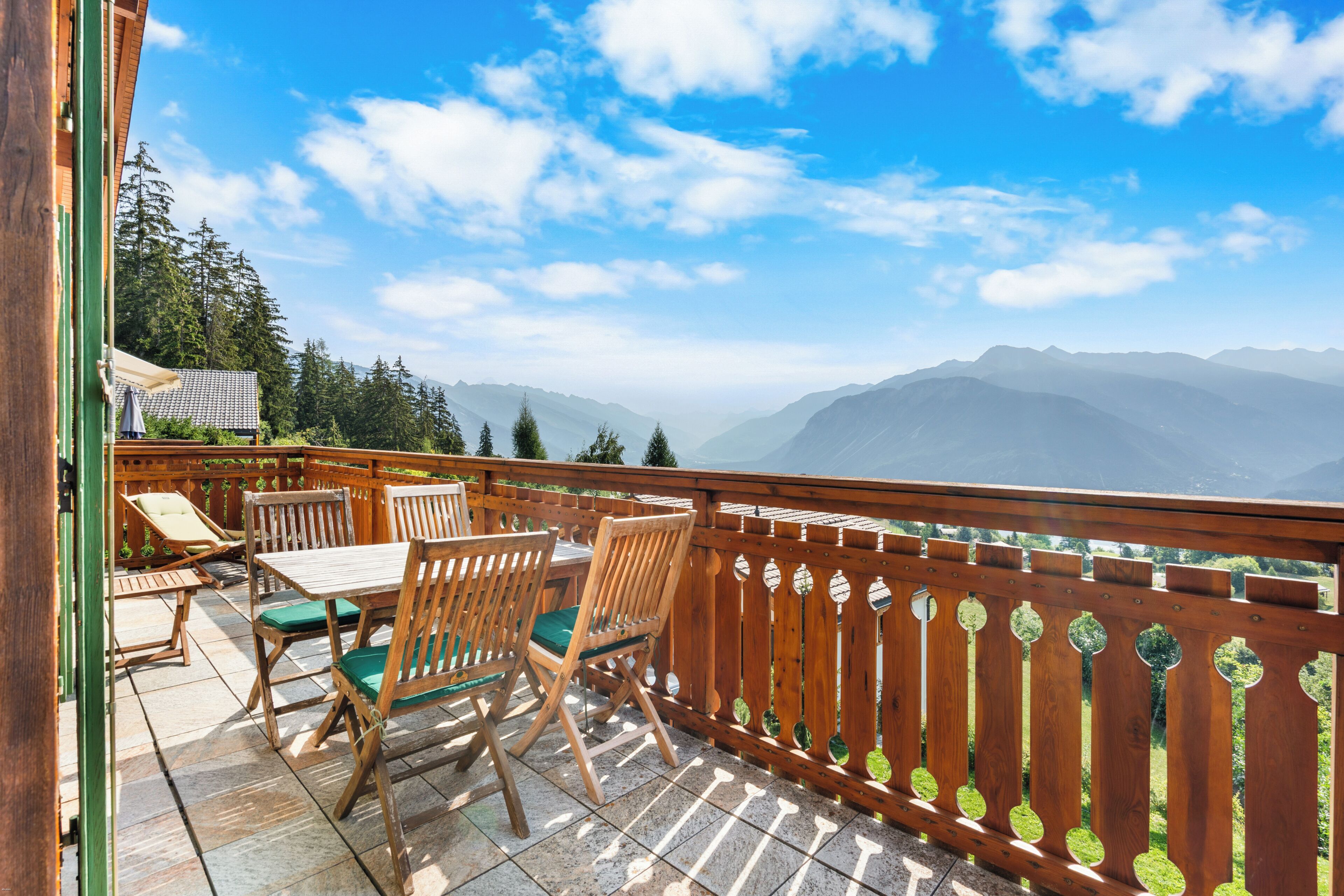 Eine Holzterrasse mit Gartenmöbeln, Blick auf Berge und einen klaren Himmel.