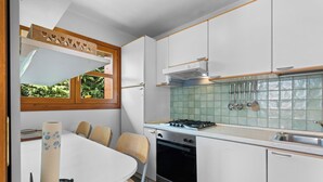 Une cuisine compacte avec des meubles blancs, une cuisinière à gaz et une fenêtre donnant sur un espace verdoyant.