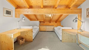 Une pièce avec un plafond en pente, des poutres en bois, deux lits, un bureau et une chaise.