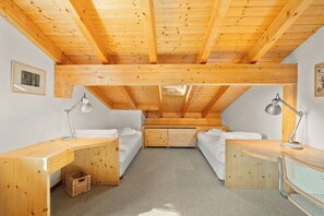 Ein Zimmer mit schrägen Wänden, Holzbalken, zwei Betten, einem Schreibtisch und einem Stuhl.