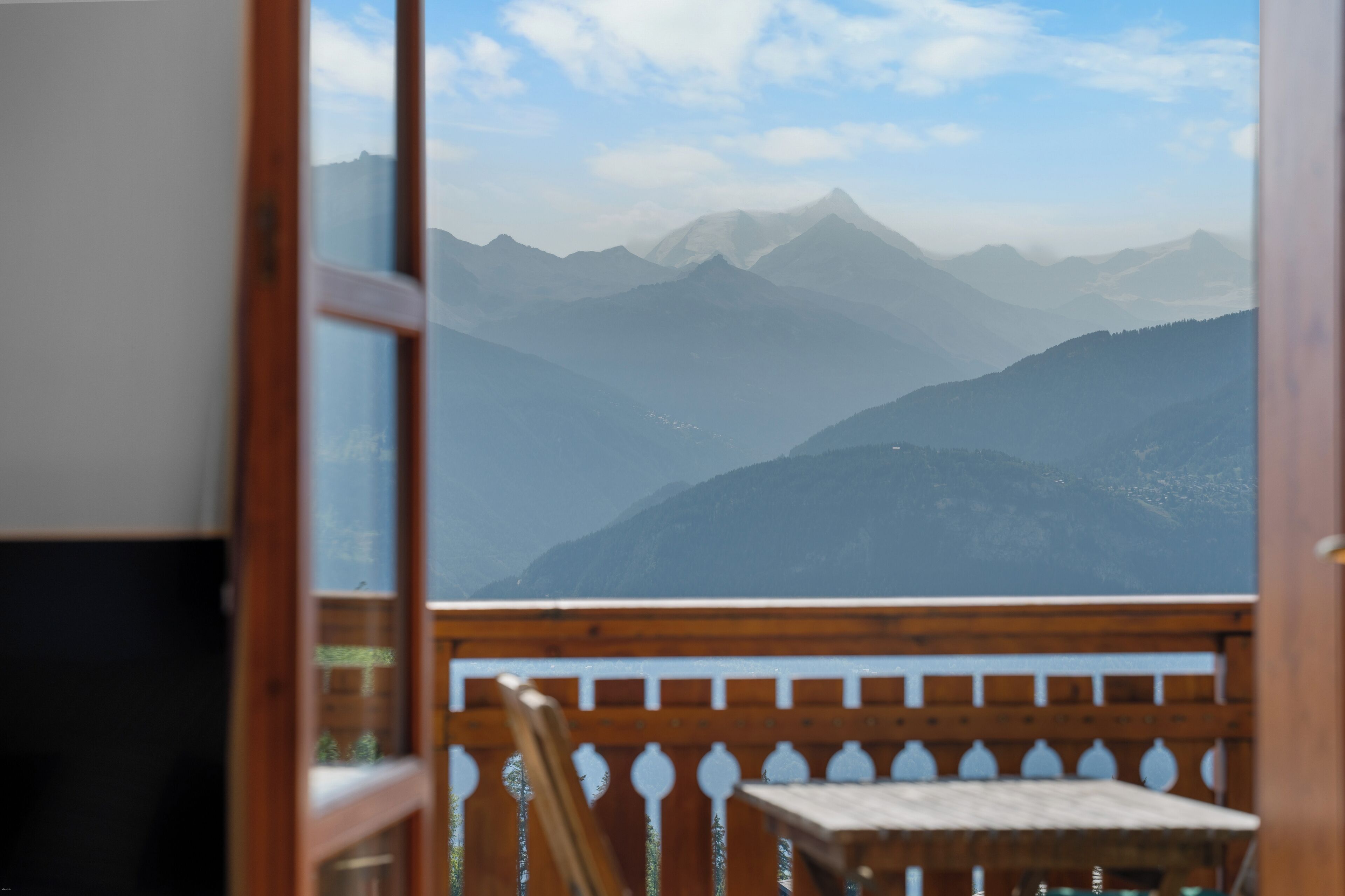 Blick vom Balkon mit Holzgeländer und Tisch auf ein Gebirge.