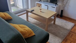 A living room with a sofa, a coffee table, a TV on a stand, a clock on the wall, and a sliding glass door. - Cozy and enjoyable apartment in Essen for a relaxing getaway (Essen)