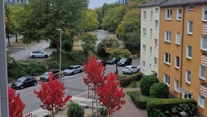A parking area with cars, a building with multiple windows, and a tree with red leaves. - Cozy and enjoyable apartment in Essen for a relaxing getaway (Essen)