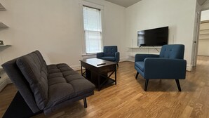 Een woonkamer met een hoekbank, twee fauteuils, een salontafel en een flatscreen-televisie.