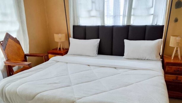 Cama bem arrumada com edredom branco acolchoado, cabeceira escura estofada e mesas de cabeceira de madeira com abajures.
