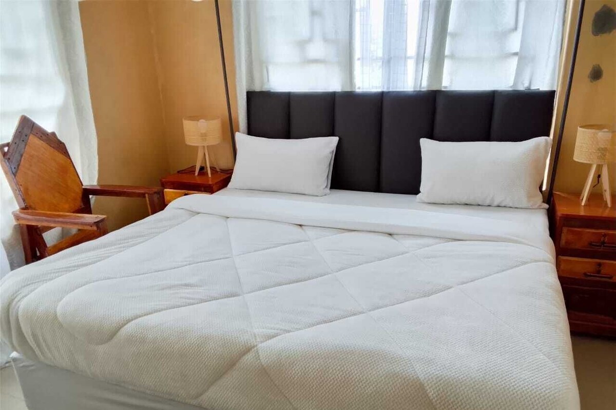 A neatly made bed with a quilted white duvet, a dark upholstered headboard, and wooden nightstands with lamps.