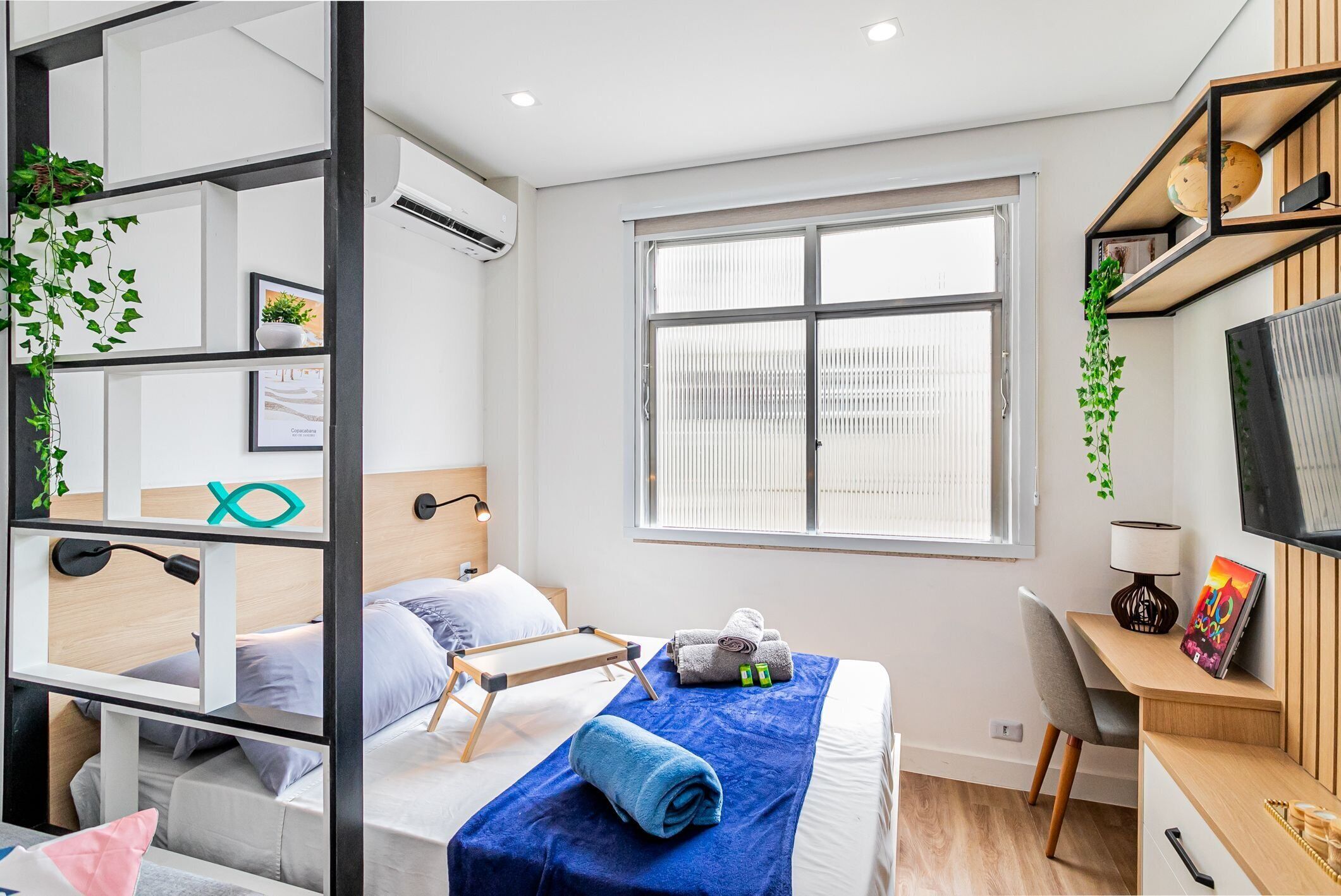 A modern hotel room with a bed, a desk, and a large window.