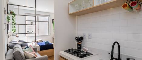 A compact kitchen with a gas stove, a sink, and a countertop. There is a sofa and a dining area visible in the background.