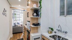 Cocina compacta con microondas, cafetera y lavabo. Hay un pequeño armario y una planta en la encimera.