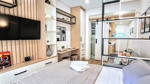 Habitación de hotel moderna con cama, televisor, escritorio con silla y armario.