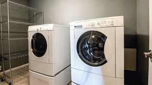 Two stacked front-loading washing machines in a laundry room with a metal shelving unit. - House in Cozy Old Town Scottsdale with AC, Pool Table, Central Location (Scottsdale)