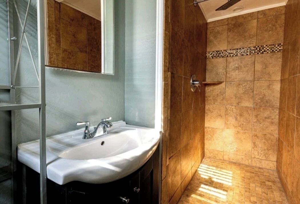 Un baño con lavamanos blanco, un espejo y una zona de ducha con paredes de azulejos.