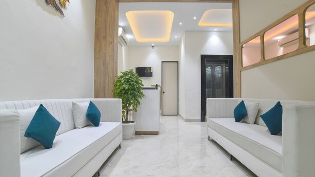 Una hall d'albergo moderna con due divani bianchi, una pianta in vaso e la reception.