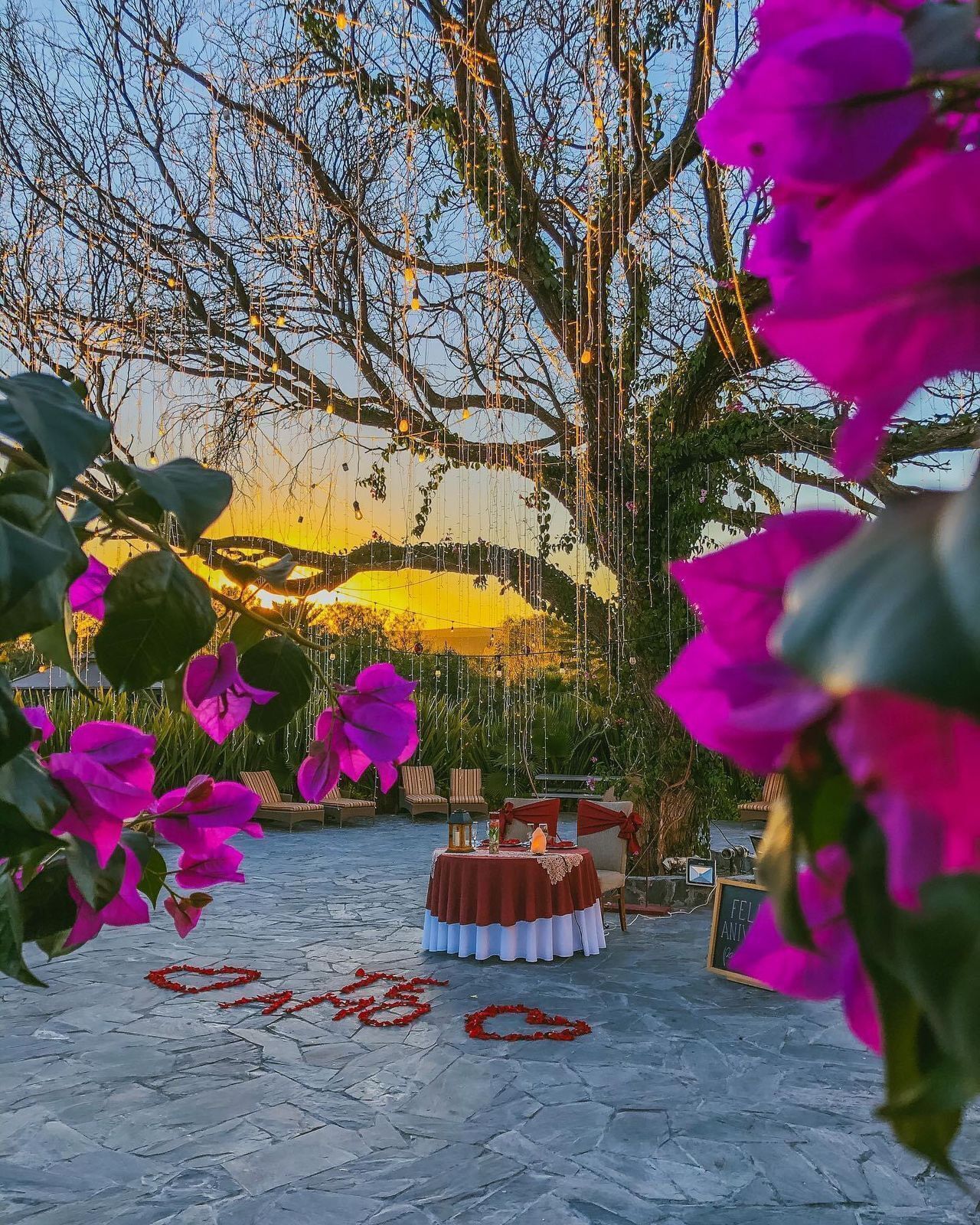 An outdoor seating area with a table set for two, surrounded by chairs and a decorative tablecloth.
