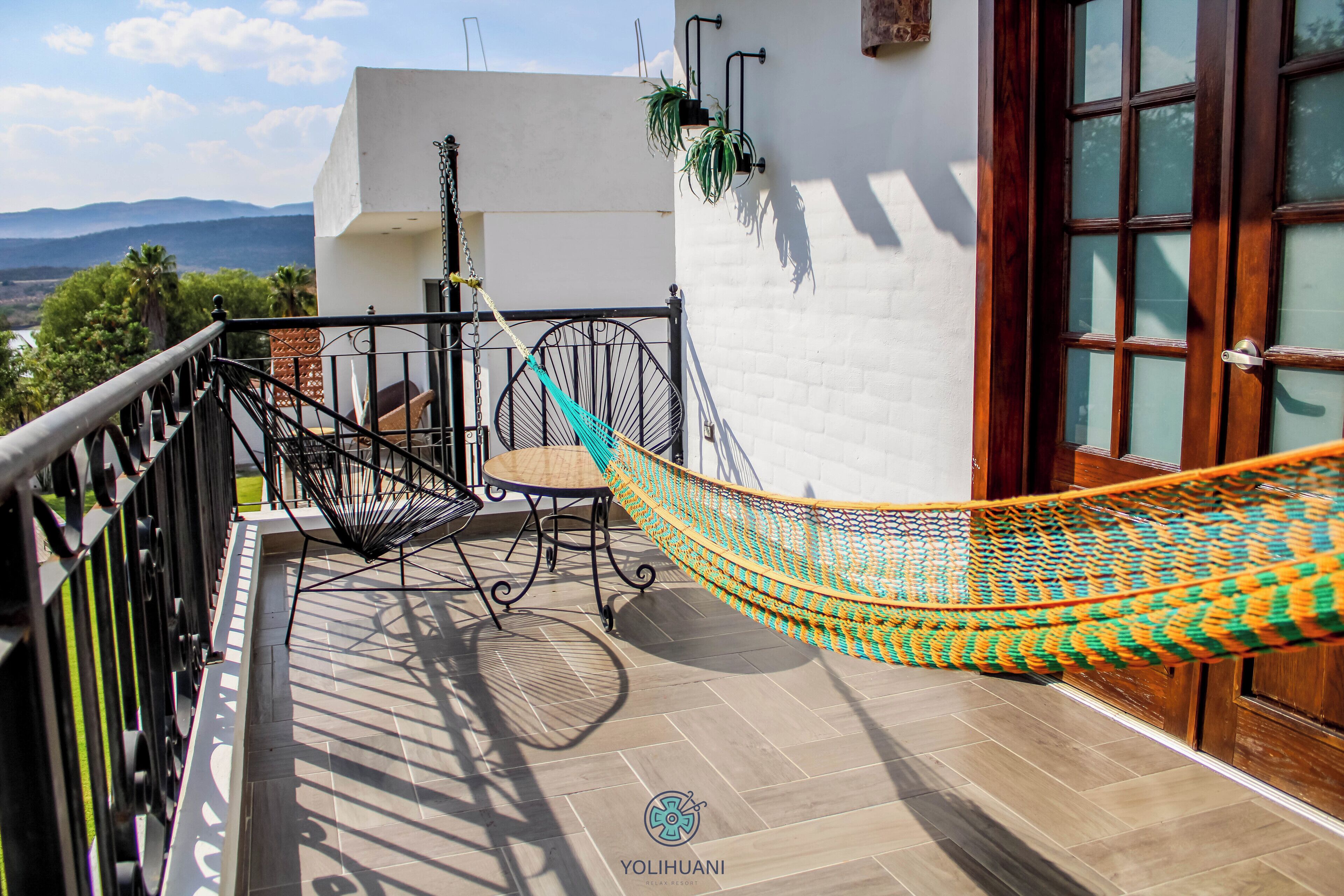 A hammock on a balcony with a view of mountains, a white wall, and a door.