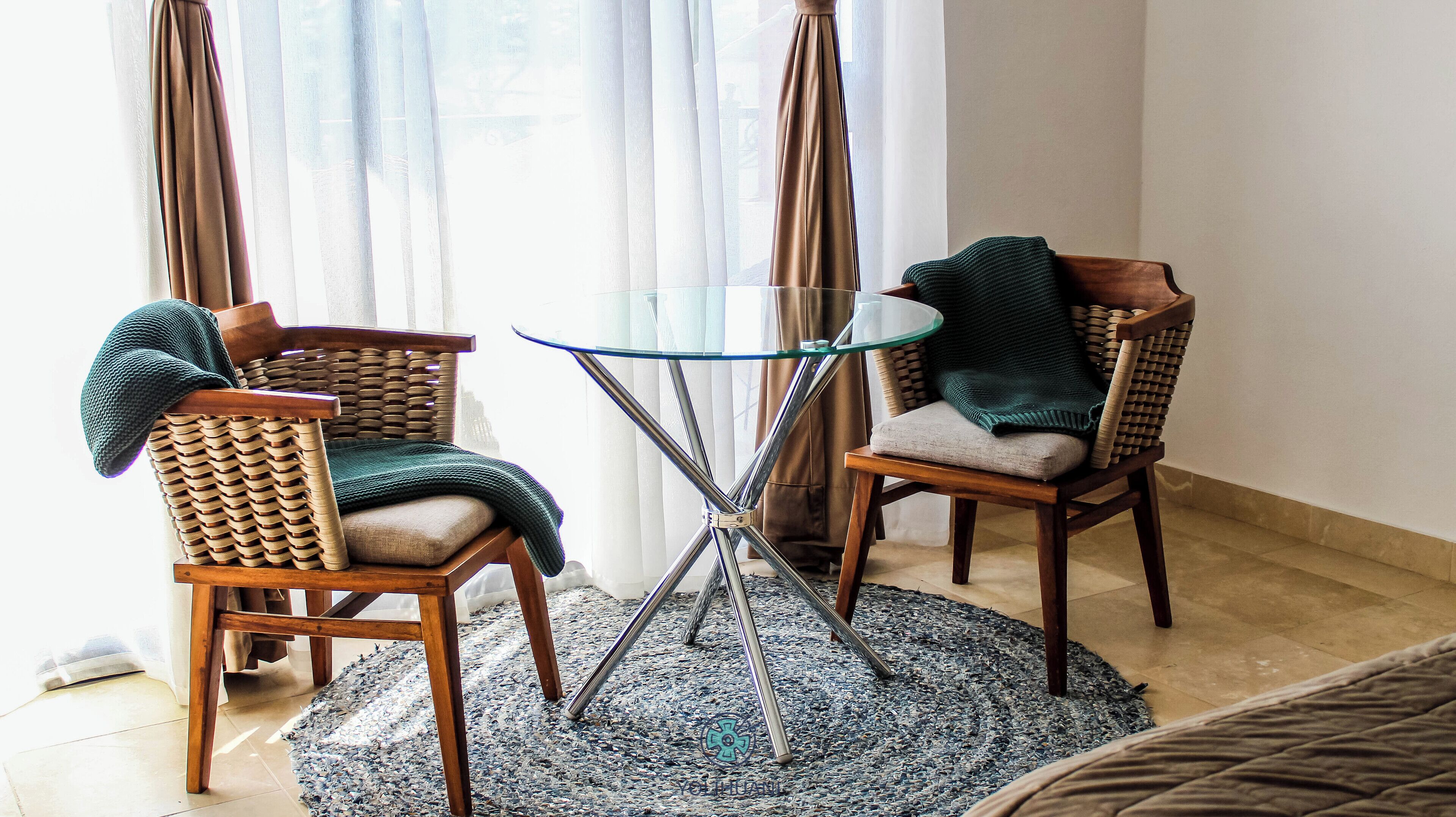 A room with two wicker chairs, a glass table, and a patterned rug.