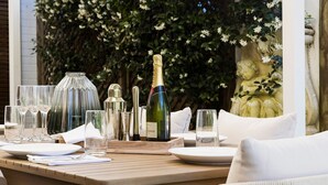 A table set for dining outdoors with a bottle of champagne, glasses, and a decorative centerpiece. - La Luce - Coastal Retreat in Port Stephens (Corlette)